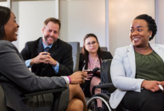 A diverse group of four leadership professionals, including a person in a wheelchair, smiling and talking together.