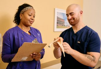 A male and a female Clinical Support staff stand together, examining an anatomical model.