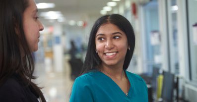 A female nurse smiles as she talks to another staff member.