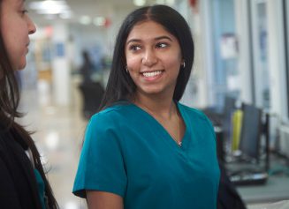 A female nurse smiles as she talks to another staff member.