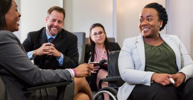 A group of four leadership professionals, including a person in a wheelchair, smiling and talking together.