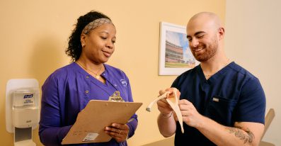 A male and a female Clinical Support staff stand together, examining an anatomical model.