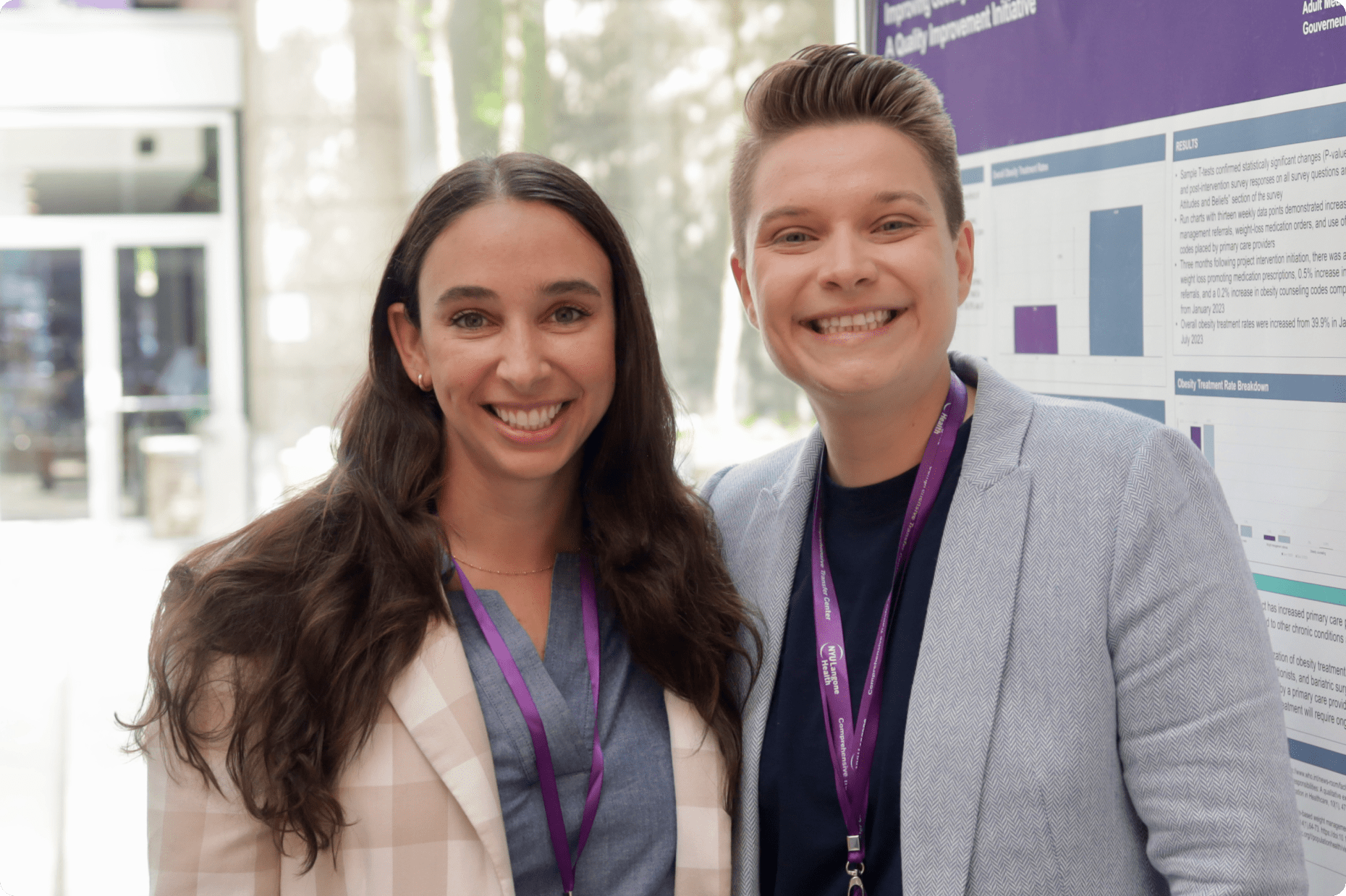 Two young staff members stand together, smiling in the modern lobby of an NYU Langone Hospital.