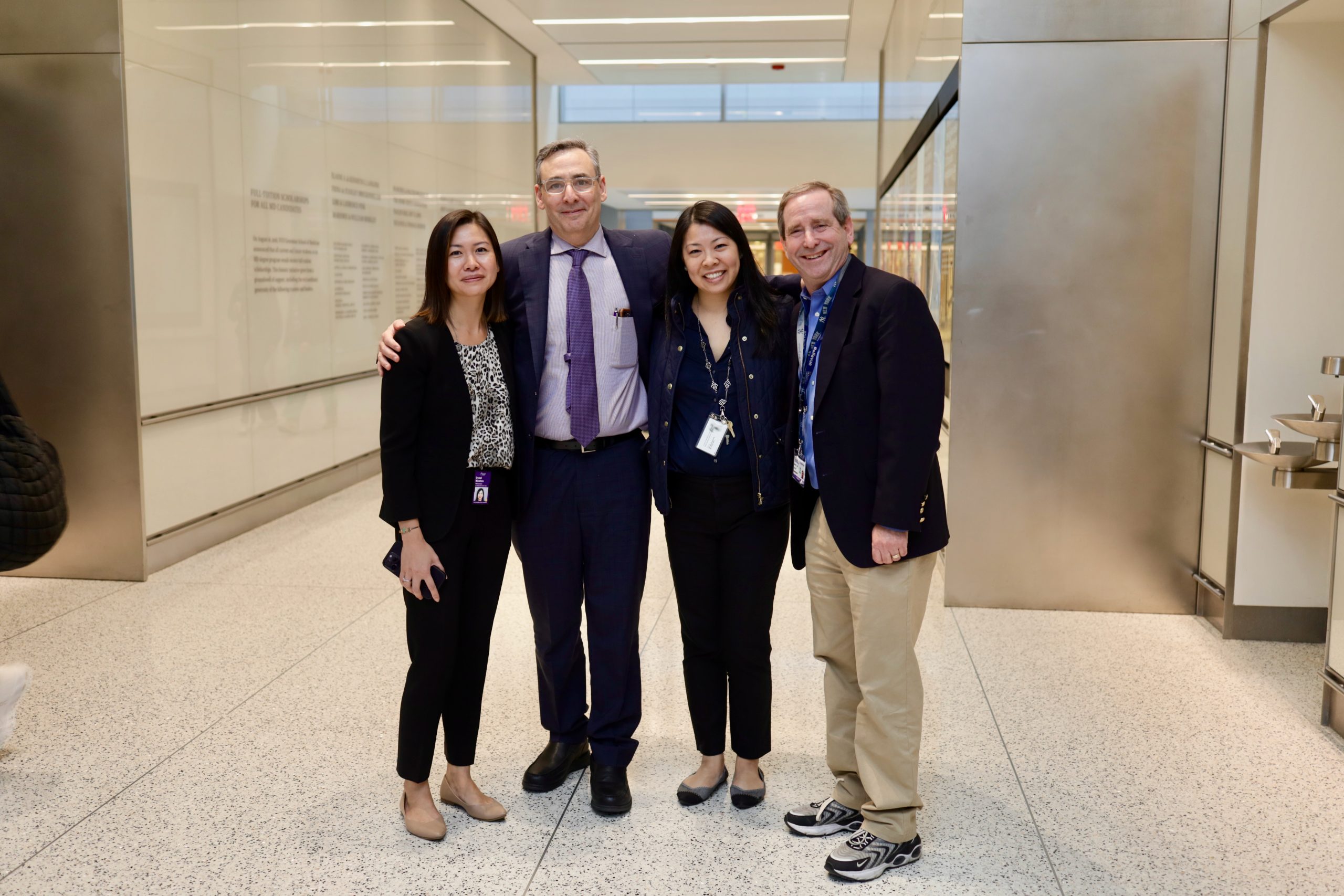 Four professionally dressed individuals stand together in a modern indoor hallway.