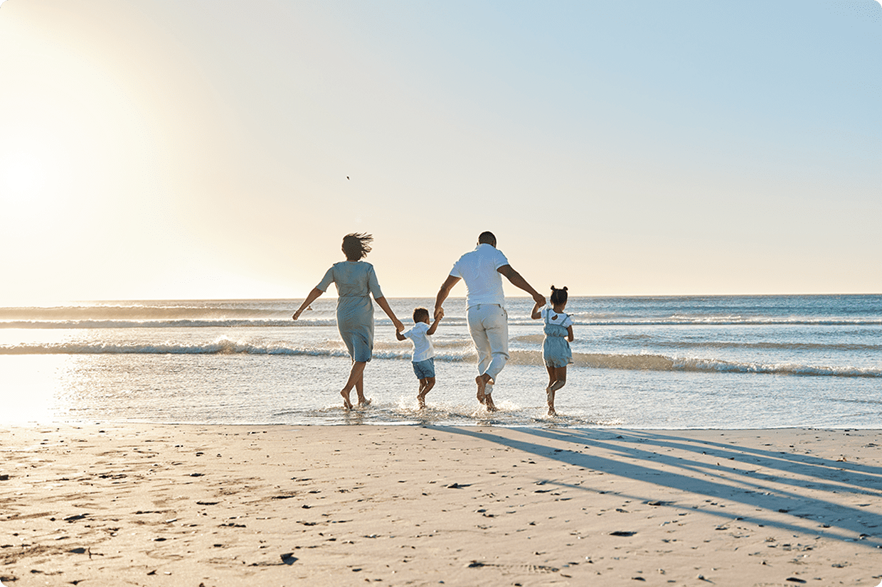 A young family holding hands and walking on the beach, heading towards the sea.