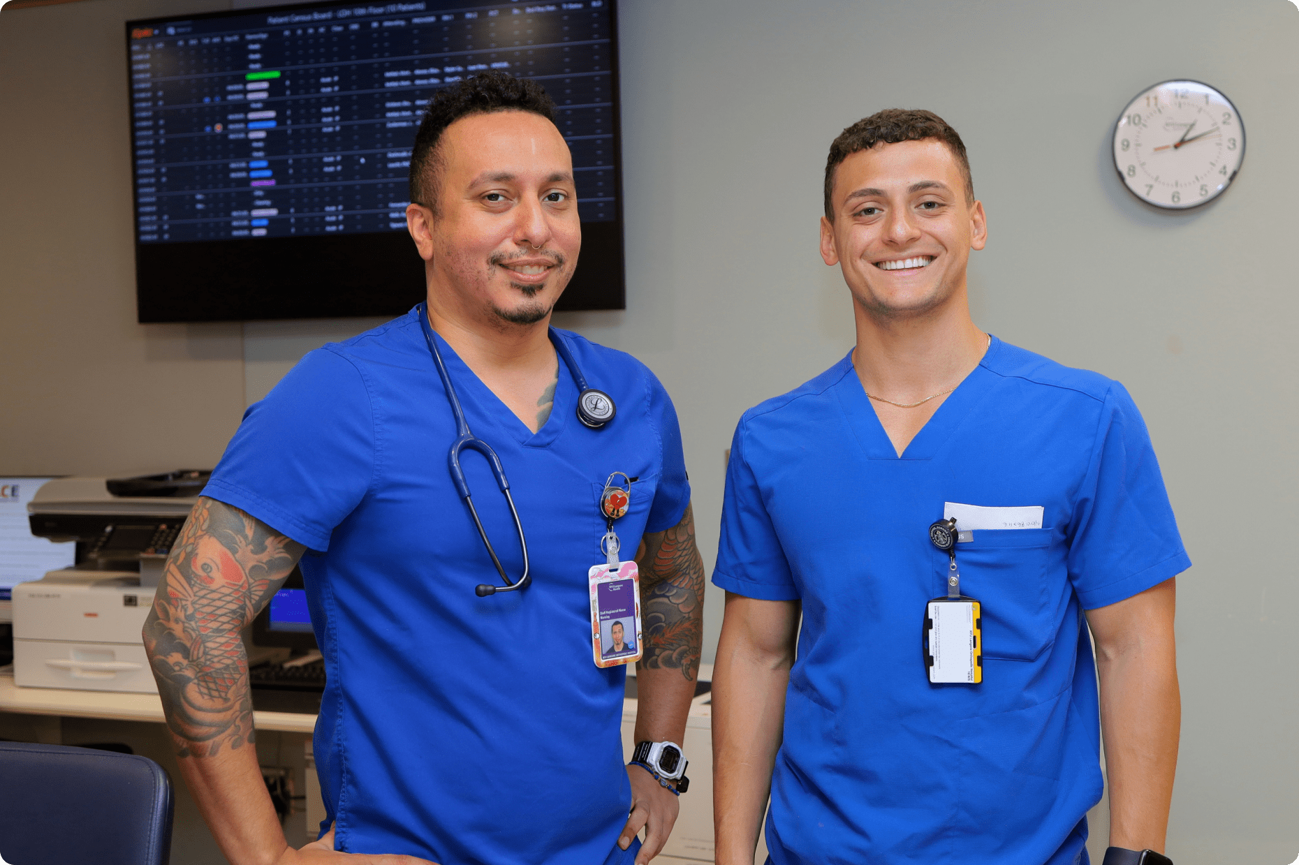 Two male NYU Langone nursing staff members stand together smiling in a hospital ward setting.