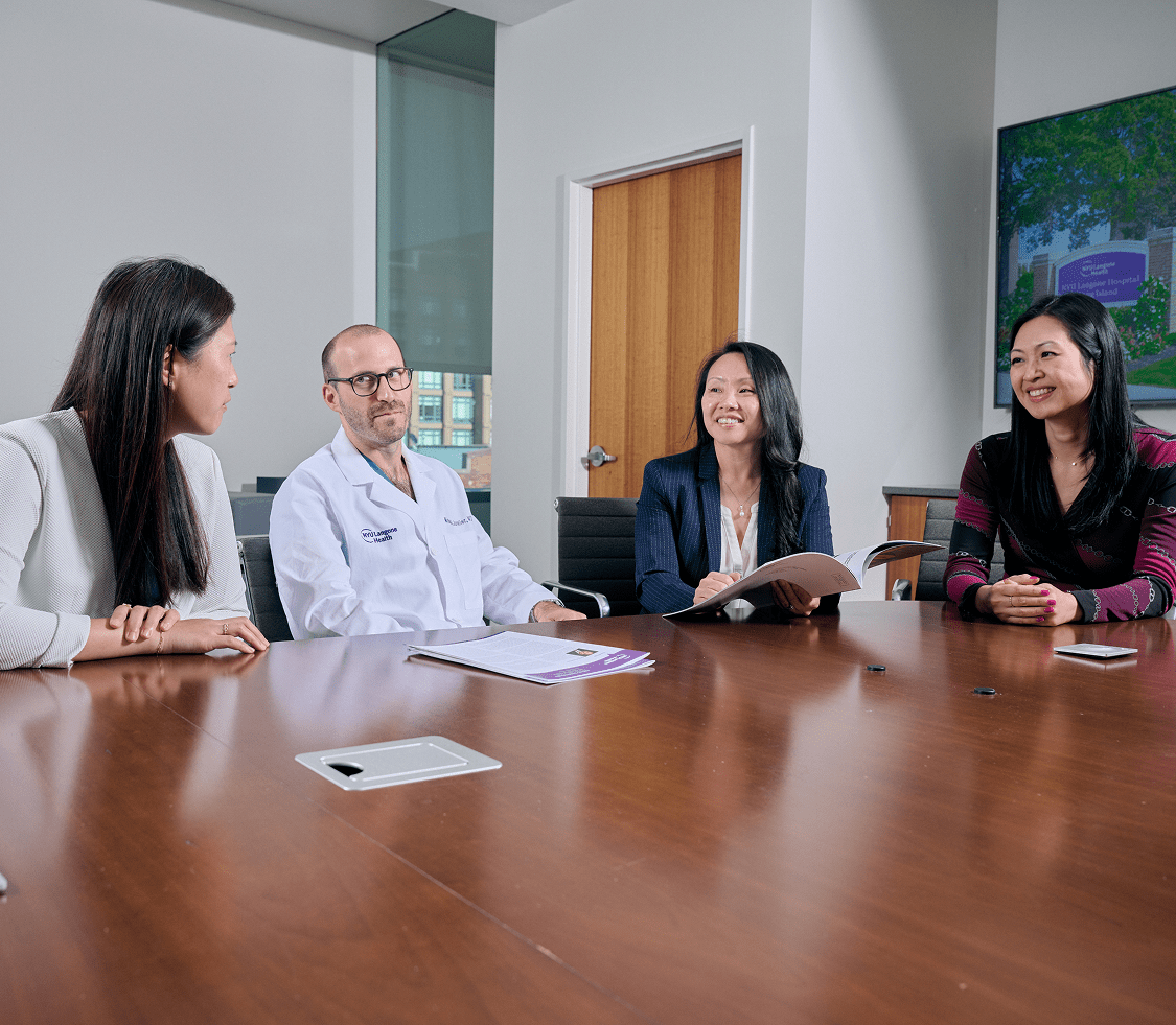 Four staff members from NYU Langone Hospital—Long Island sit at a conference room table, working together.