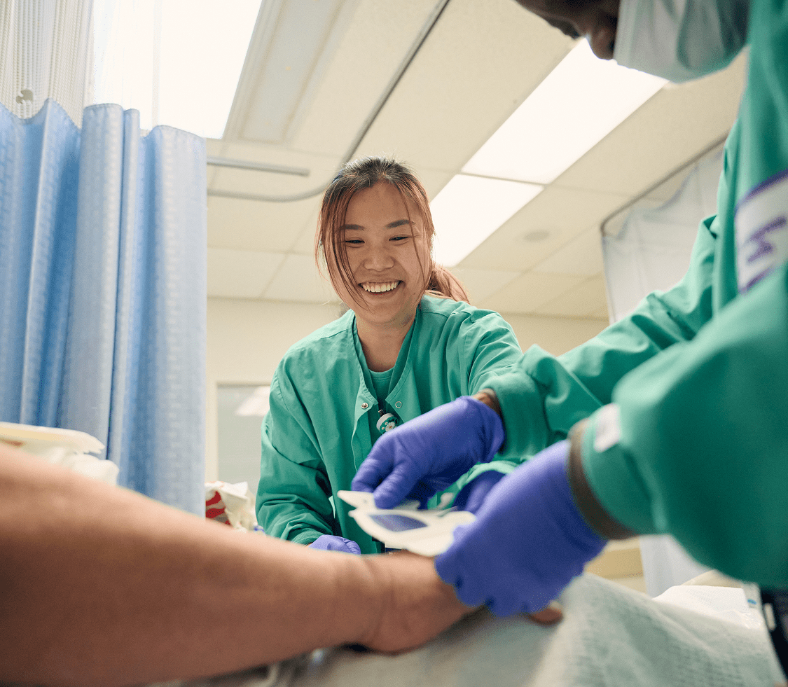 Two medical staff members from NYU Langone Hospital—Long Island provide treatment for a patient at their bedside.
