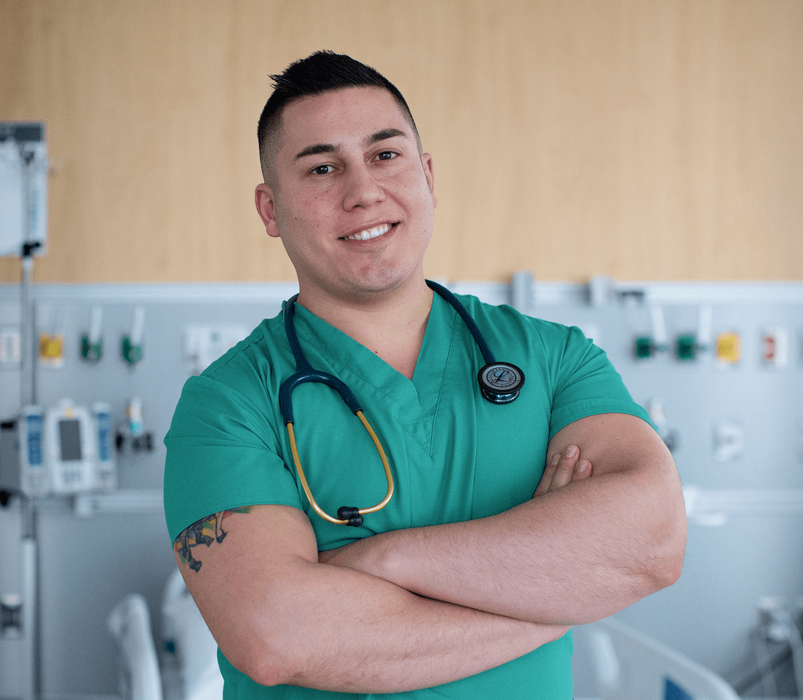 A male medical staff member from NYU Langone Hospital—Long Island stands smiling in a hospital ward setting.