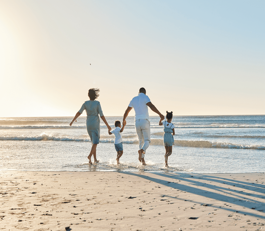 A young family holding hands and walking on the beach, heading towards the sea.
