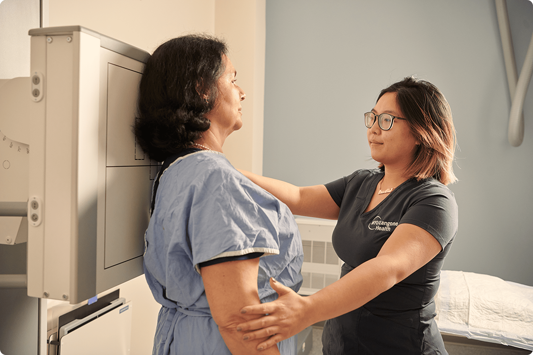 A female staff member from NYU Langone Hospital—Long Island positions a female patient in front of an X-ray machine.
