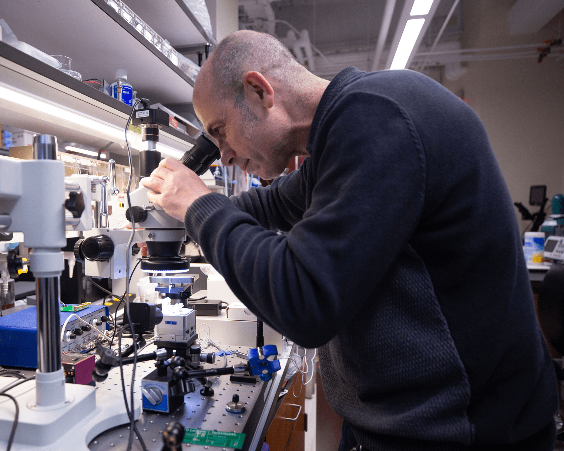 A researcher at NYU Langone looks down a microscope in a laboratory.
