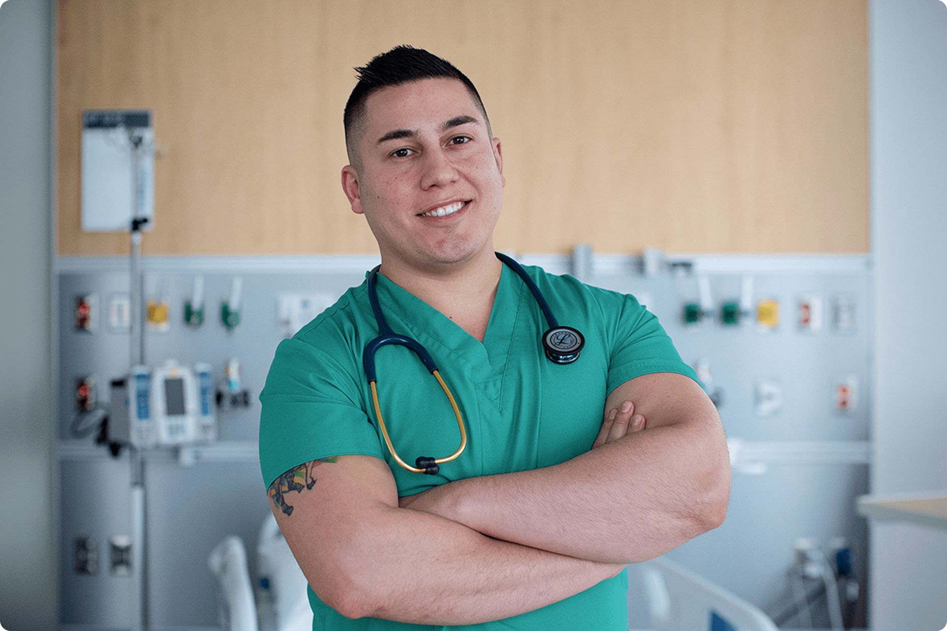A male medical staff member from NYU Langone Hospital—Long Island stands smiling in a hospital ward setting.