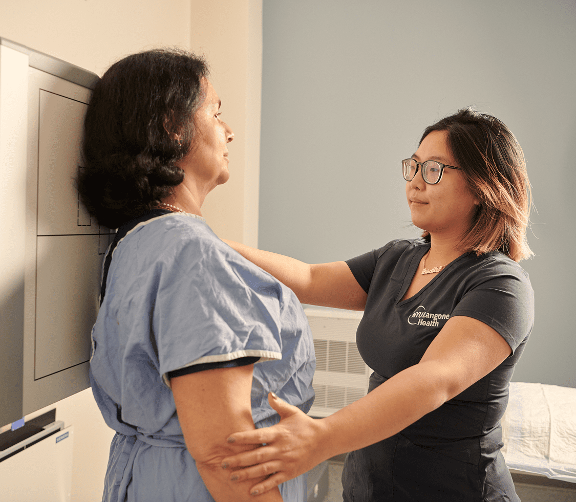 A female staff member from NYU Langone Hospital—Long Island positions a female patient in front of an X-ray machine.
