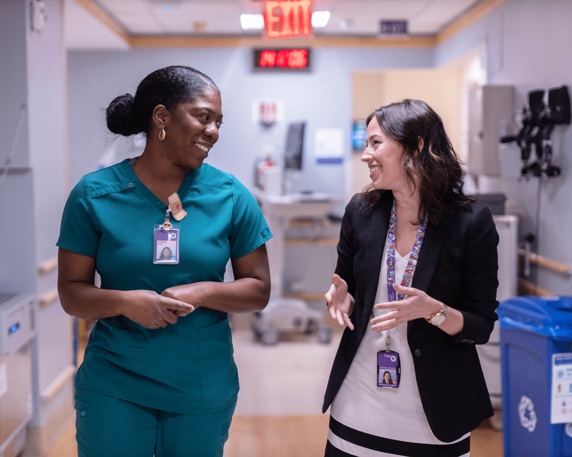 Two female nursing staff at NYU Langone walk and talk together in a hospital ward.