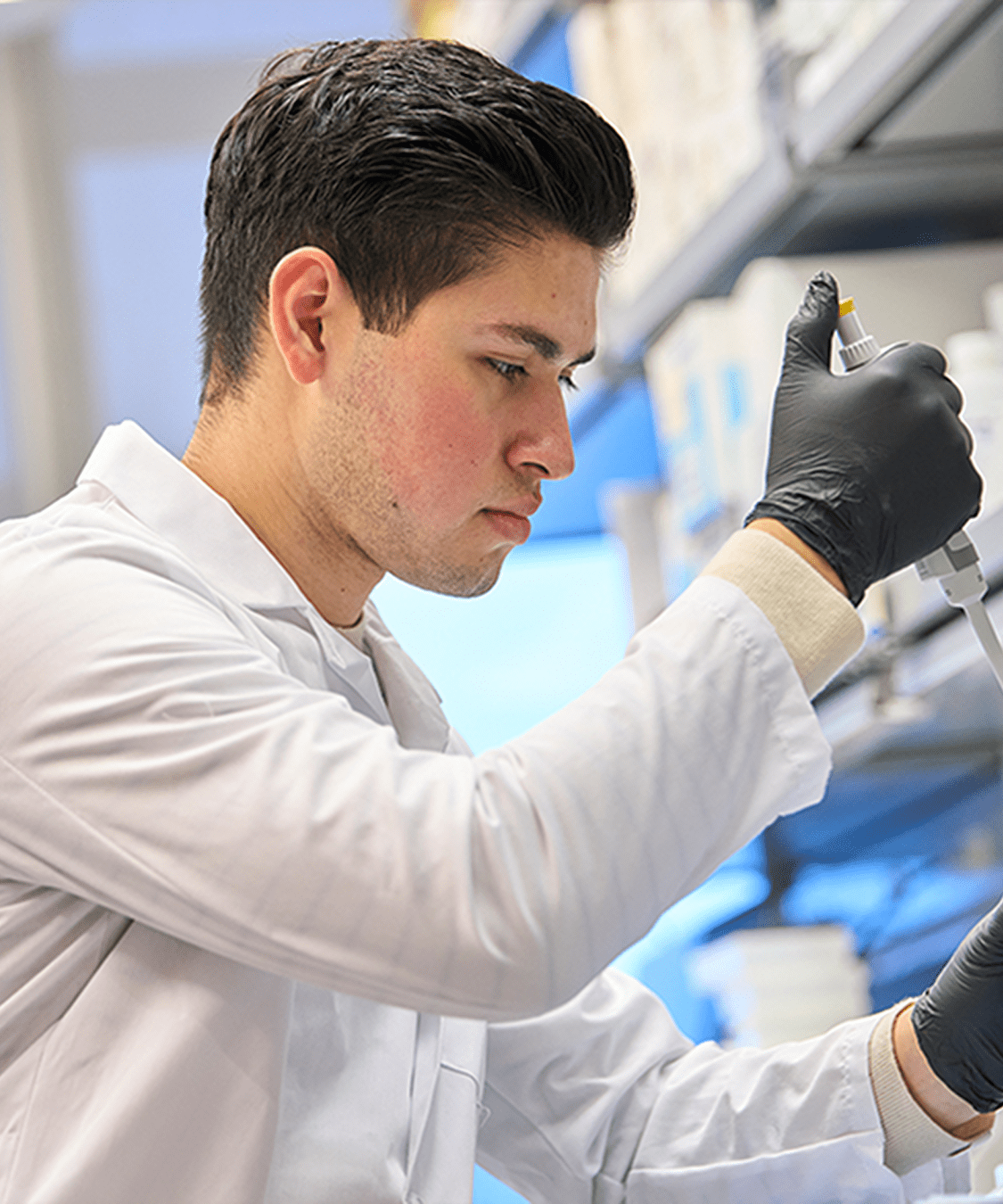 A male staff member at NYU Langone works in a laboratory, holding a pipette and test tube.