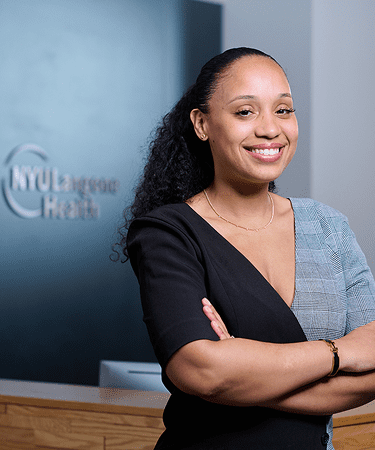 A female staff member at NYU Langone stands smiling with her arms crossed.