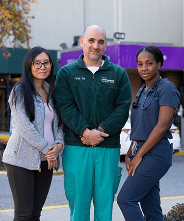Three staff members stand proudly outside the NYU Langone Hospital—Brooklyn building.