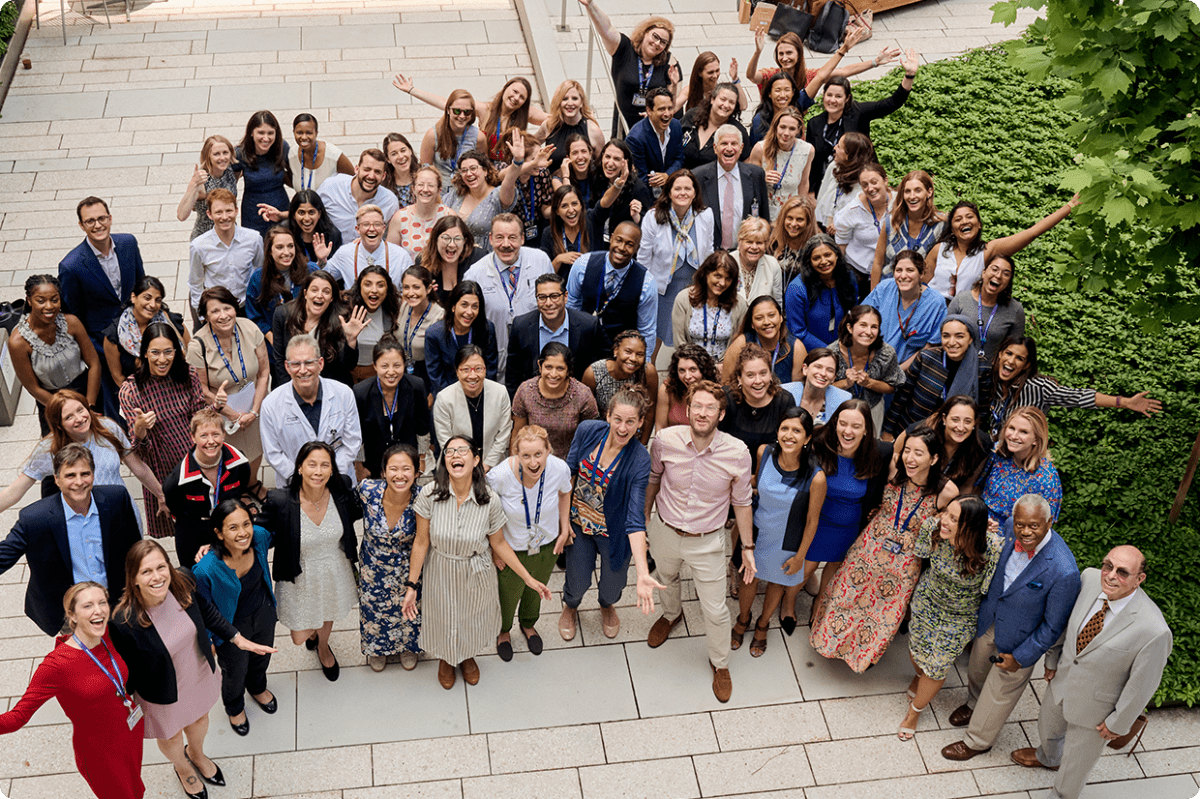 A group of NYU Langone professionals gathers outdoors on a paved walkway with greenery.