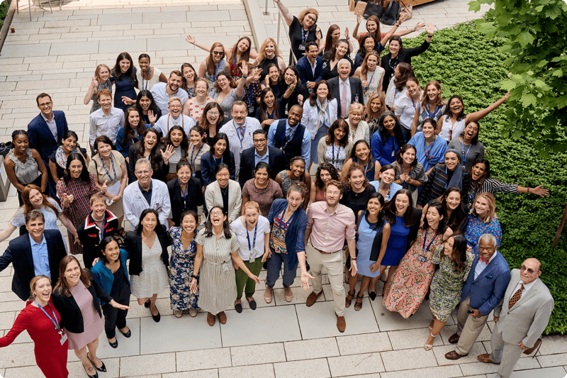 A group of NYU Langone professionals gathers outdoors on a paved walkway with greenery.