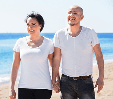 A man and a woman holding hands while walking on a beach.