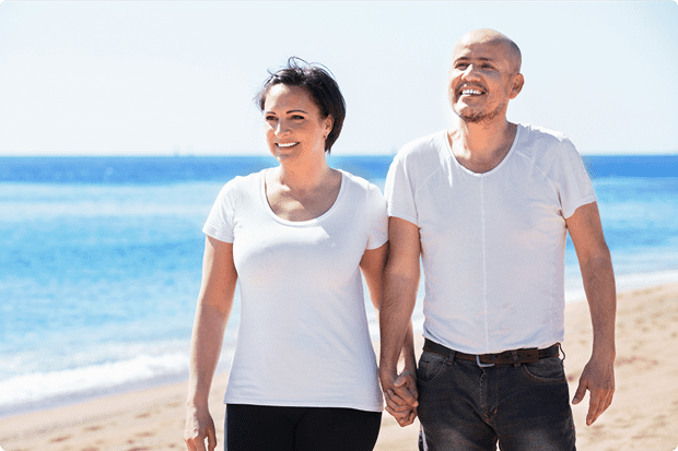 A man and a woman holding hands while walking on a beach.