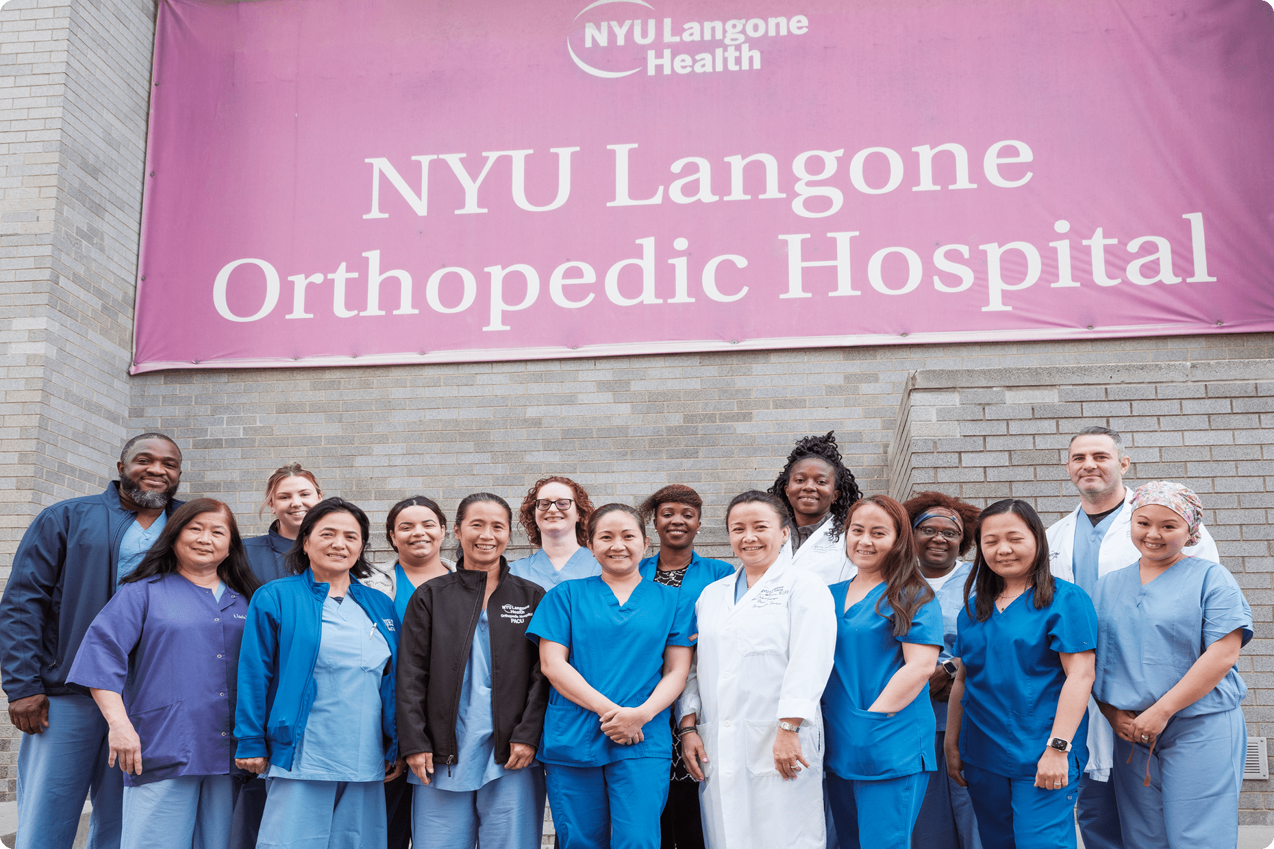 A group of staff members stand underneath a large NYU Langone Orthopedic Hospital banner outside the building.
